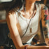 Person wearing a beige tank top with visible tattoos on arms, sitting indoors.
